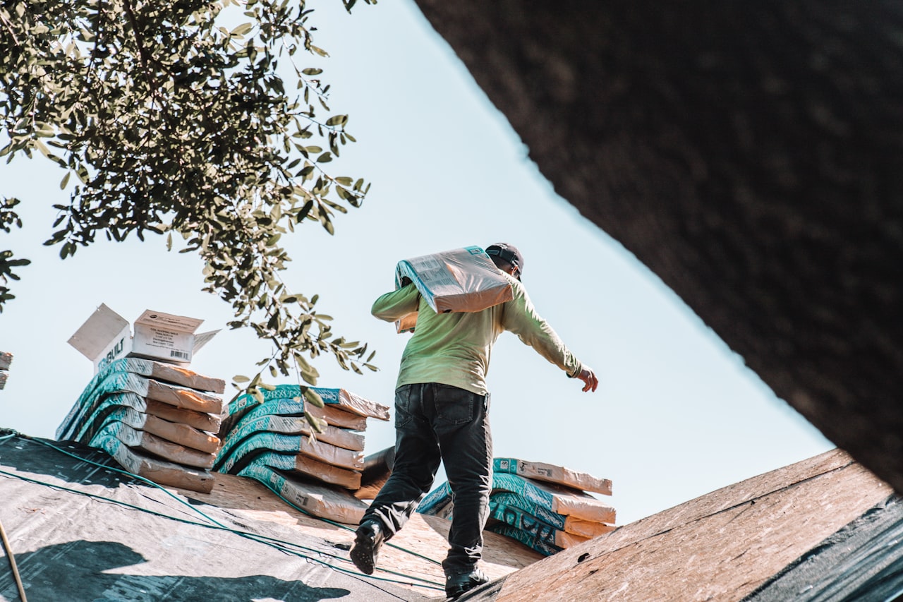 Roofer carrying a bundle of shingles up to a roof on a clear day